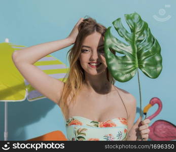 smiling young woman swimsuit standing with monstera leaf studio