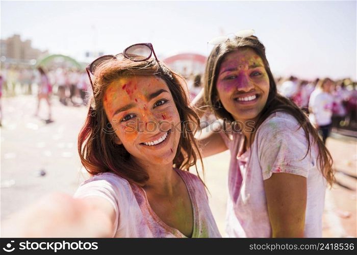 smiling young woman taking selfie with her friend holi