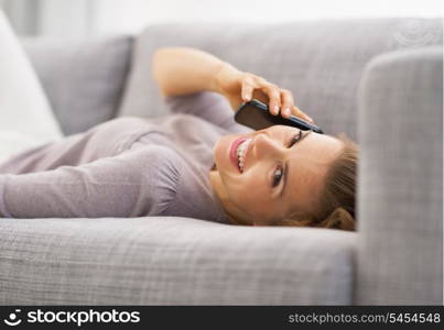 Smiling young woman talking mobile phone while laying on couch