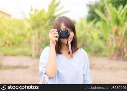 Smiling young woman using a camera to take photo outdoors at the park