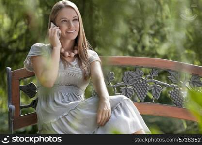 Smiling young woman using mobile phone on park bench