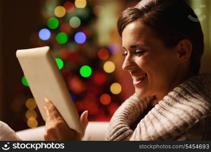 Smiling young woman using tablet pc in front of christmas tree