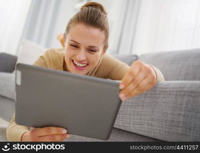 Smiling young woman using tablet pc while laying on sofa