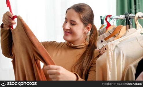 Smiling young woman walking in shopping mall or boutique and choosing dress to buy. Woman doing shopping on season sale.. Smiling young woman walking in shopping mall or boutique and choosing dress to buy. Woman doing shopping on season sale