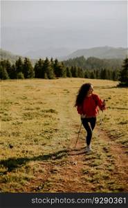 Smiling young woman walking with backpack over green hills