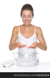 Smiling young woman washing hands in glass bowl with water