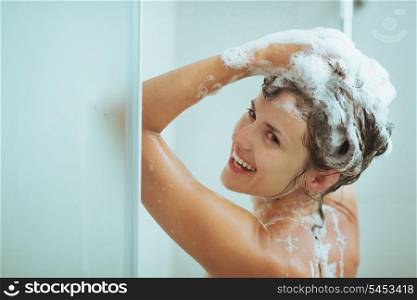 Smiling young woman washing head with shampoo