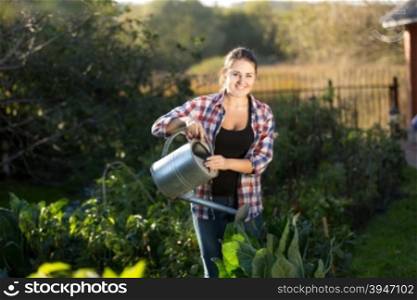Smiling young woman watering plants at garden at sunny day