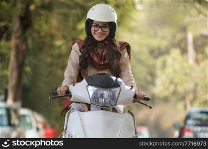 Smiling young woman wearing eyeglasses and helmet riding scooter.
