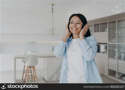Smiling young woman wearing wireless headphones listening to modern music at home. Happy female listen to favorite song, podcast audio book in headset, relaxing, enjoying perfect sound quality.. Woman wearing headphones listen to music, podcast or audio book enjoying perfect sound at home