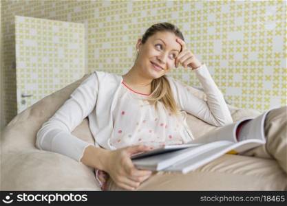 Smiling young woman with books sitting on couch at home