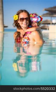 Smiling young woman with child playing in swimming pool. Summer vacations concept