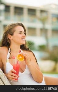 Smiling young woman with cocktail laying on chaise-longue