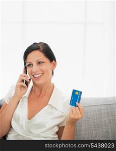 Smiling young woman with credit card and speaking mobile phone