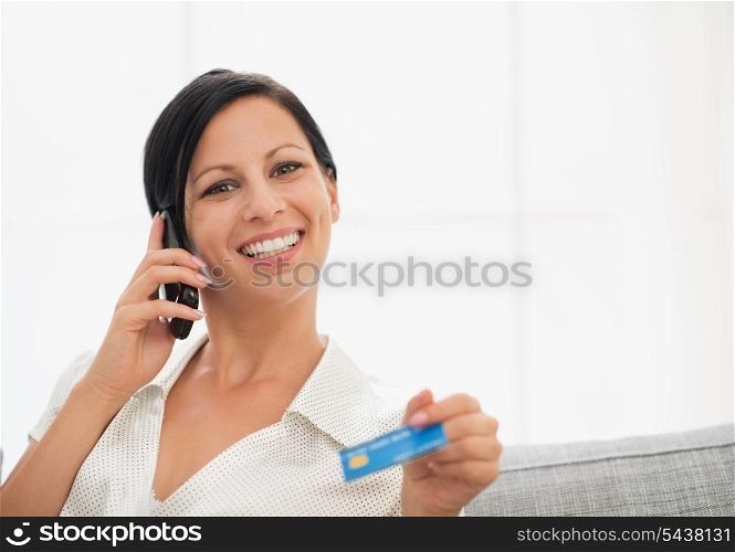 Smiling young woman with credit card speaking mobile