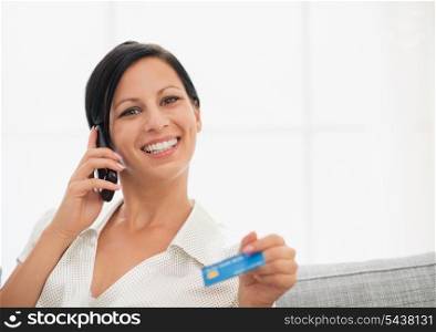 Smiling young woman with credit card speaking mobile