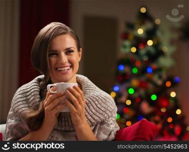Smiling young woman with cup of hot chocolate in front of Christmas lights