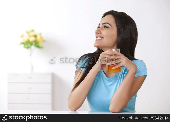 Smiling young woman with glass of orange juice at home