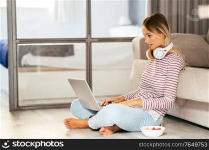 Smiling young woman with headphones and laptop on the sofa at home.. Smiling young woman with headphones and laptop on the sofa