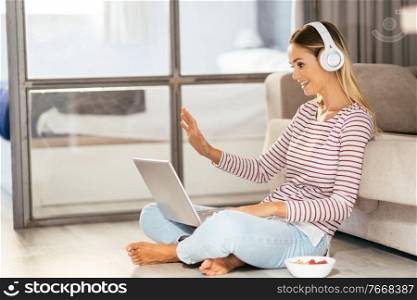 Smiling young woman with headphones and laptop videoconferencing on the sofa at home.. Smiling young woman with headphones and laptop on the sofa
