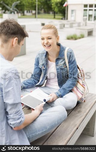 Smiling young woman with male friend studying on bench at college campus
