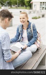 Smiling young woman with male friend studying on bench at college campus