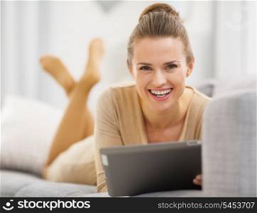 Smiling young woman with tablet pc laying on sofa