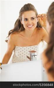 Smiling young woman with tweezers in bathroom