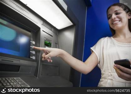 Smiling young woman withdrawing money from the ATM