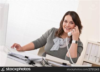 Smiling young woman working on the phone at office