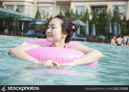 Smiling young women in the pool with an inflatable tube, looking away