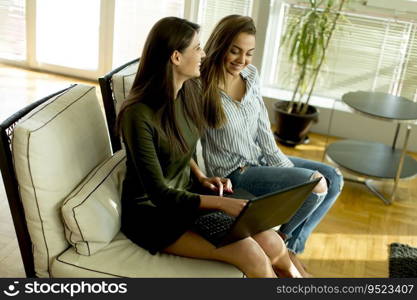 Smiling young women sitting on sofa relaxing while browsing online shopping website