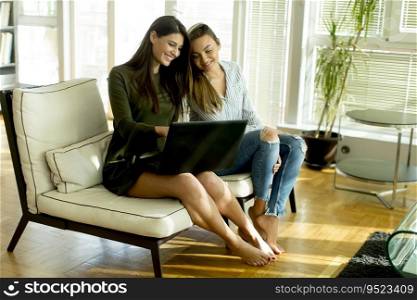 Smiling young women sitting on sofa relaxing while browsing online shopping website