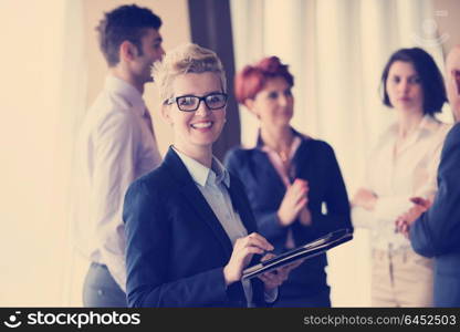 Smilling senior older business woman with tablet computer in front her team blured in background. Group of young business people at modern bright startup office interior.