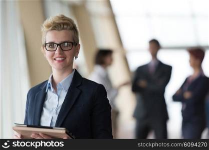 Smilling young business woman with tablet computer in front her team blured in background. Group of young business people. Modern bright startup office interior.