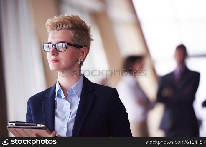 Smilling young business woman with tablet computer in front her team blured in background. Group of young business people. Modern bright startup office interior.