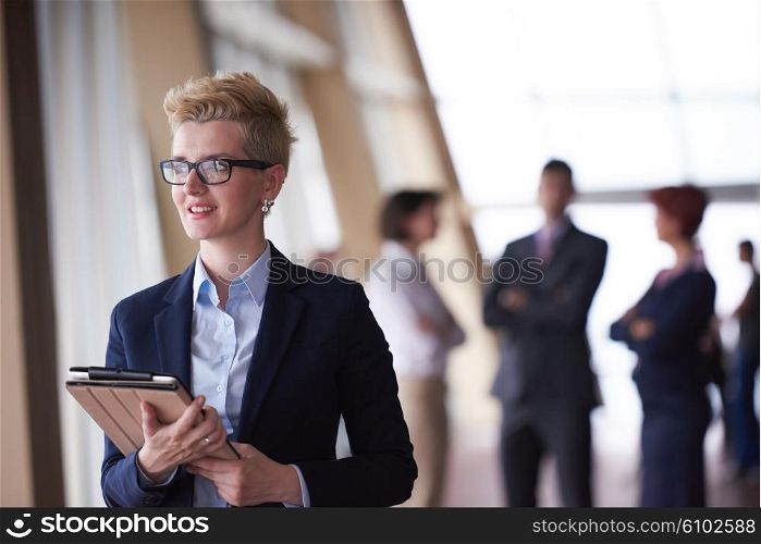 Smilling young business woman withglassess tablet computer in front her team blured in background. Group of young business people. Modern bright startup office interior.