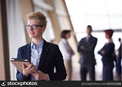 Smilling young business woman withglassess tablet computer in front her team blured in background. Group of young business people. Modern bright startup office interior.