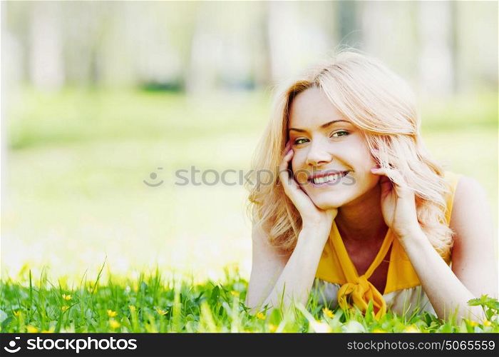 Smilng happy young woman lying on green grass meadow. Young woman on grass