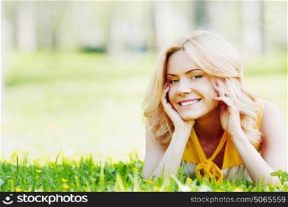 Smilng happy young woman lying on green grass meadow. Young woman on grass