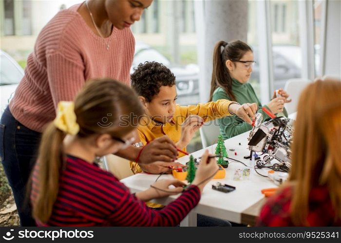 Smily African American female science teacher with group of kids programming electric toys and robots at robotics classroom