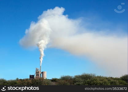 Smoke from an industrial plant drifting in the wind against a blue sky