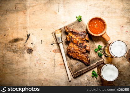 Smoked barbecue ribs with tomato sauce and cold beer. On wooden background.. Smoked barbecue ribs with tomato sauce and cold beer.