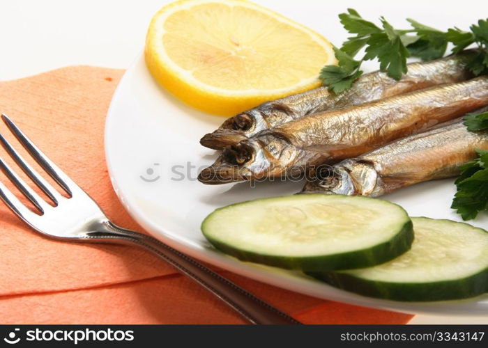 Smoked fishes with lemon, cucumber and green parsley on white plate. Close-up. Studio photography.