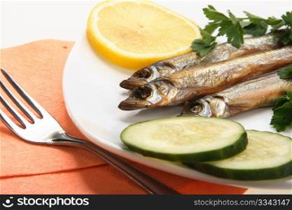 Smoked fishes with lemon, cucumber and green parsley on white plate. Close-up. Studio photography.