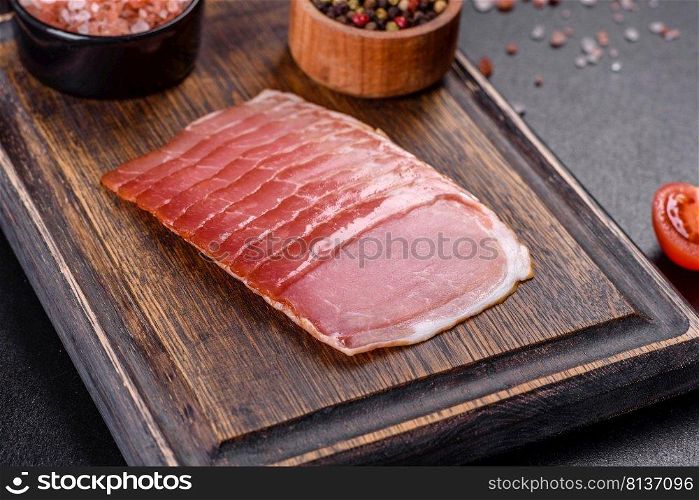 Smoked ham on a dark concrete table with addition of fresh aromatic herbs and spices, natural product from organic farm. Smoked ham on a dark concrete table with addition of fresh aromatic herbs and spices