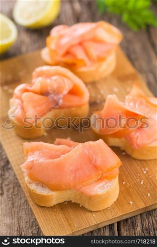 Smoked salmon slices on baguette on wooden board (Selective Focus, Focus on the first salmon slice) . Smoked Salmon on Baguette