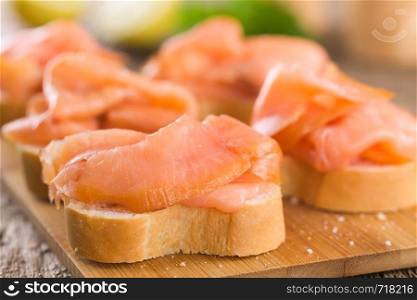 Smoked salmon slices on baguette on wooden board (Selective Focus, Focus one third into the first salmon slice) . Smoked Salmon on Baguette