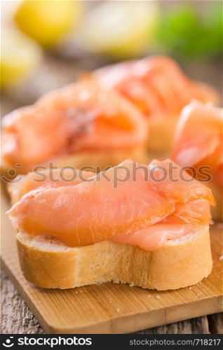 Smoked salmon slices on baguette on wooden board (Selective Focus, Focus one third into the image) . Smoked Salmon on Baguette