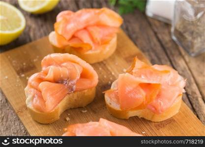 Smoked salmon slices on baguette on wooden board (Selective Focus, Focus one third into the image) . Smoked Salmon on Baguette